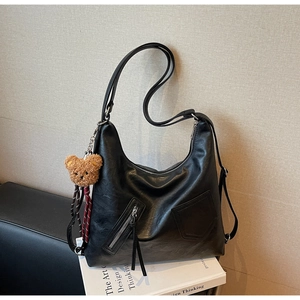Detail of black matte leather hobo bag with zip pocket and cute brown teddy bear charm