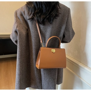 Détail d'un sac bandoulière en cuir marron avec fermoir tournant doré et coutures fines