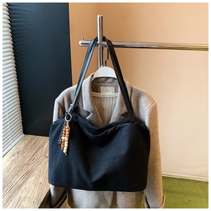 Detail view of black canvas tote bag with colorful beaded tassel on a suit hanger