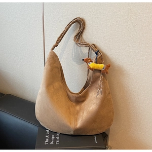 Detail of a brown suede hobo bag with a woven shoulder strap and cute dachshund charm