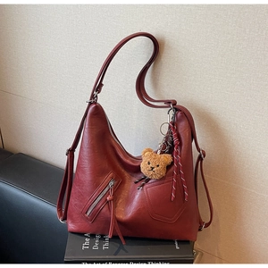 Macro detail of dark red faux leather backpack featuring zipper pockets and plush bear charm