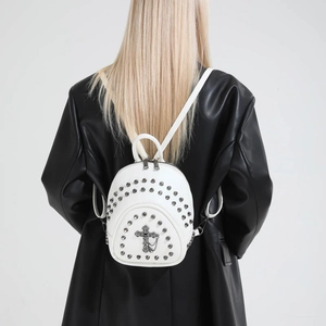 Detailed view of a white mini rivet backpack with a metal cross charm on a black coat