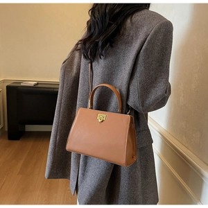 Detailed back view of a camel leather crossbody bag on a grey coat with gold lock