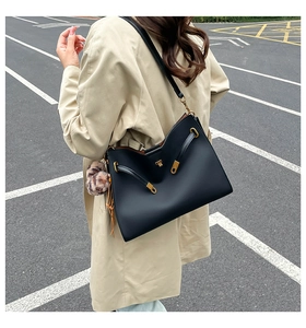 Close-up of black leather tote bag featuring a gold twist lock and a brown fur pompom charm