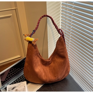 Brown suede hobo bag with red woven handle and dachshund plush charm on office desk