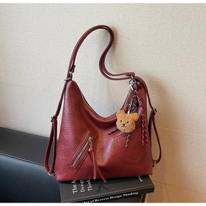 Detail of vintage dark red leather backpack with side pocket and cute bear charm decor