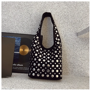 Détail du sac hobo en daim noir avec rivets métalliques argentés sur fond industriel