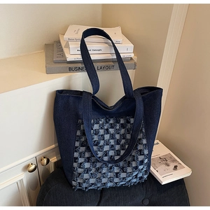 Gros plan d'un sac cabas en denim bleu foncé avec un design patchwork à carreaux frangés