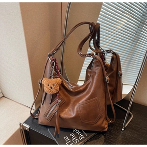 Detailed view of brown retro leather tote bag featuring a plush bear charm and side zip pocket