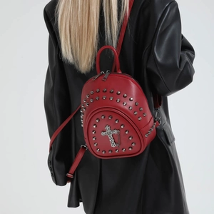 Detail of red punk mini backpack with silver rivets and metal cross on black leather jacket