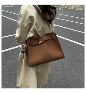 Detail view of brown leather tote bag with gold lock and leopard print pompom charm