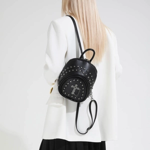Detail of a black mini studded backpack featuring a metal cross and chains on a model
