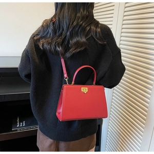 Detail of red structured crossbody bag with gold lock buckle and leather handle