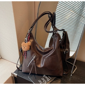 Detail of dark brown faux leather tote bag with zip pockets and a cute plush bear charm