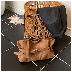 Close-up of brown suede tote bag featuring adjustable strap and metallic buckle detail