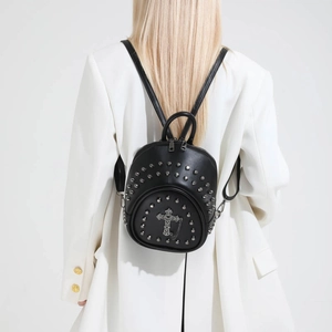 Detail of black mini studded leather backpack with ornate silver cross and metal chain decoration