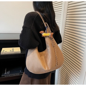 Brown suede hobo bag with a yellow dachshund plush charm shown in a warm lifestyle setting