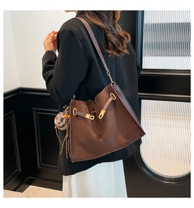 Detail of dark brown suede bucket bag with drawstring, metal buckle and plush pom-pom charm