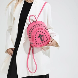Detail of bright pink mini backpack with dark metal rivets and silver cross pendant