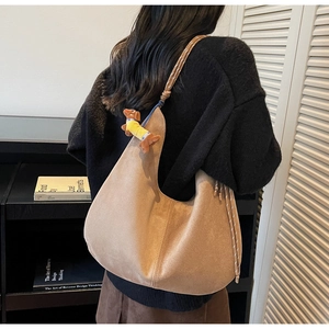 Close-up of a warm brown suede hobo bag featuring a woven handle and a cute dog charm