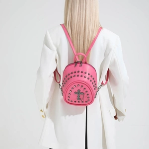Pink mini rivet backpack featuring metal cross pendant worn by model in white suit
