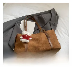 Brown suede tote bag detail with plush bear charm on white bedding with a blazer