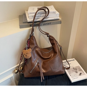 Detail of dark brown Hobo bag with fringe tassel, plush bear charm and plaid scarf accent