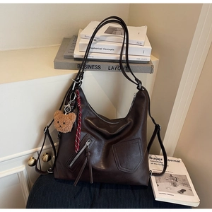 Detailed view of dark brown soft leather tote bag with stylish plush bear and woven charm