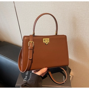 Detailed view of brown leather crossbody bag with gold heart-shaped rotating lock on books