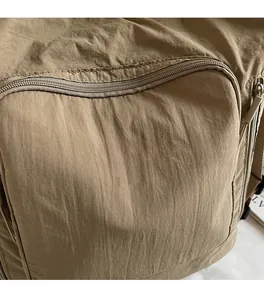 Detail of khaki nylon tote bag showing white embroidered lettering and smooth zipper texture