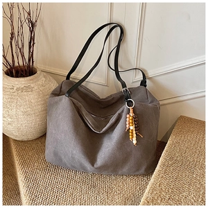 Detail of grey canvas tote bag with black leather straps and colorful wooden bead tassel