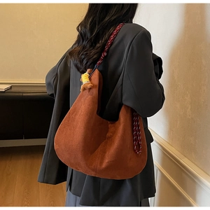 Detail view of large burgundy suede crescent bag with woven strap and bear charm