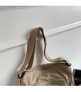 Detail of khaki shoulder bag featuring wide fabric straps and black metal buckles