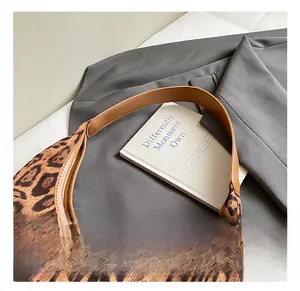 Detail of leopard print tote bag with brown leather handle on neutral background