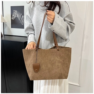 Detail of a large brown suede tote bag with leather straps and decorative charm pendant