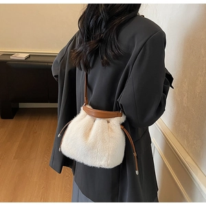 Side view of a plush white faux fur bucket bag with brown leather drawstrings and strap