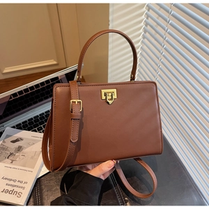 Detailed view of brown leather handbag with gold clasp on desk with magazine