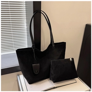 Detail of minimalist black suede tote bag and matching pouch on a desk with artistic books