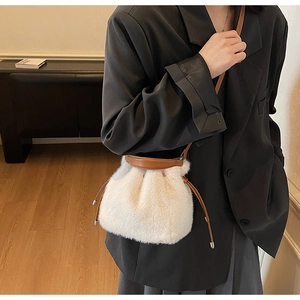 Detail of white faux fur bucket bag with brown leather drawstring and metal accents
