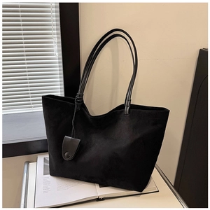 Detail of a large black suede tote bag with slim straps placed over an open magazine