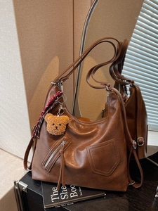 Brown large capacity leather tote bag with decorative zippers and plush bear charm