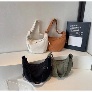 Collection of four-color canvas half-moon crossbody bags on a minimalist pedestal