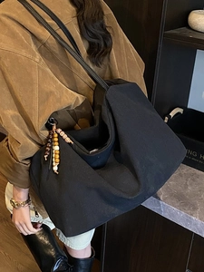 Retro black canvas tote bag with wooden bead charm worn by a model in a warm vintage setting