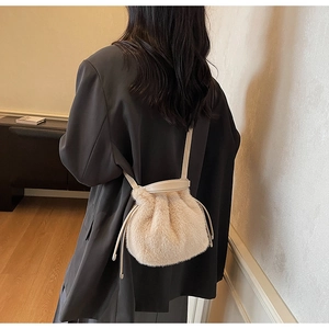 Detail view of beige plush bucket bag with drawstring closure on model in black suit