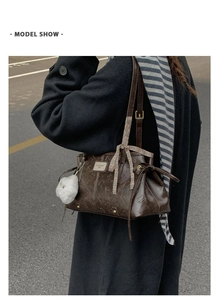 Detail of dark brown tote bag featuring embossed cat patterns and a plaid ribbon bow