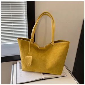Detail of yellow suede tote bag with long handles and charm on a minimalist background