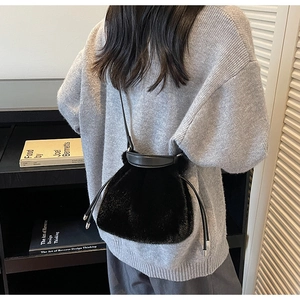 Detail showing the plush black bucket bag with leather strap and drawstring closure