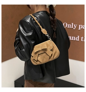 Detail of brown matte saddle bag featuring a decorative bow and woven shoulder strap