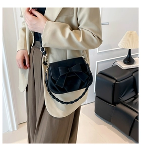 Detail view of black saddle bag with bow accent and woven handle on beige blazer
