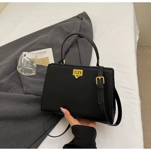Close-up of black matte leather handbag with golden geometric lock on white surface